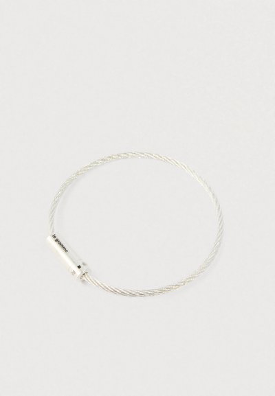 Sudraba vērpta stieples aproce ar cilindrisku aizdari, uz kuras ir iegravēts "le gramme" un "9g", uz vienkārša gaiša fona.