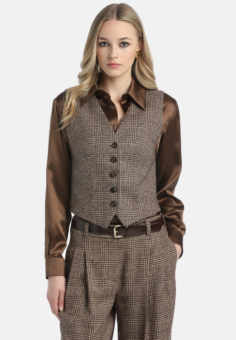 Bruine houndstooth vest met een fitted ontwerp, knoopsluiting, gedragen over een glanzende bruine blouse, gecombineerd met high-waisted geruite broek en een riem.