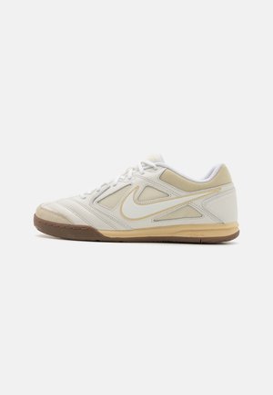 Weiße und beige Nike-Sneaker in niedrigem Schnitt mit Mesh-Einsätzen, weißen Schnürsenkeln und einer Gummisohle in Karamellfarbe, seitlich auf einfachem Hintergrund gezeigt.
