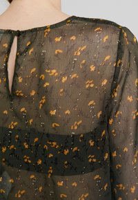 Häikäisevä vihreä paita, jossa on keltainen ja valkoinen kukkakuosi, avaimenreikä takaosassa ja pehmeä, kevyt rakenne.