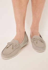 Heled hallid nubukist loafers, millel on õmmeldud muster, paelteema koos kuldsete detailidega ja paindlik valge talla.