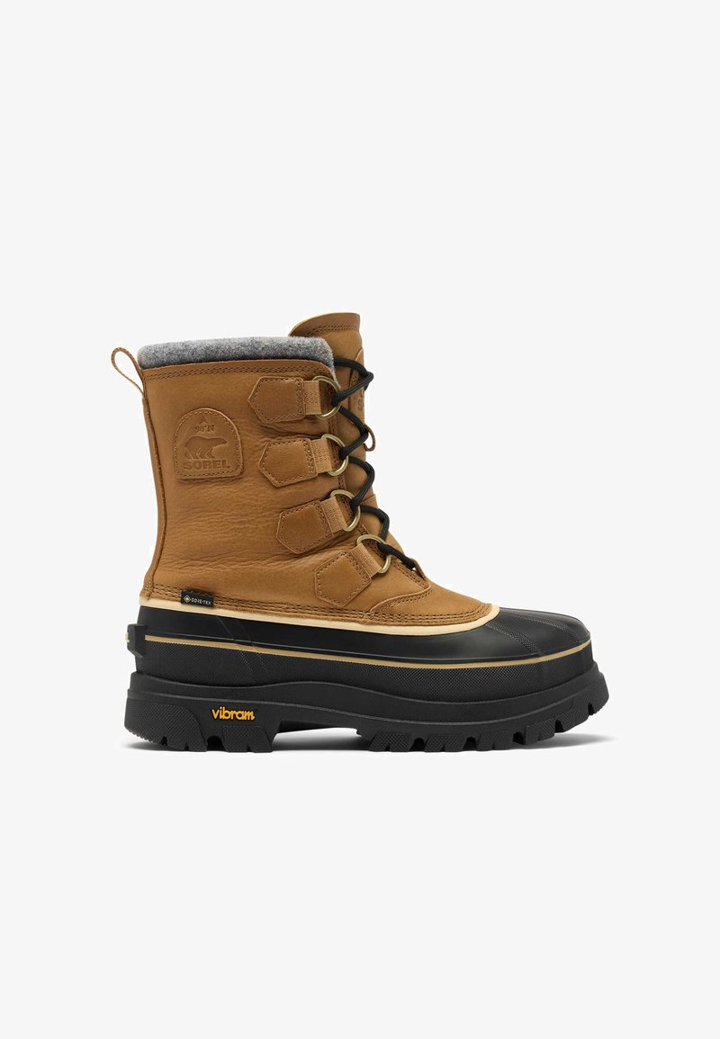 Botte en cuir beige avec un col en feutre gris, une base en caoutchouc noir, des lacets visibles et un logo Vibram au talon. Matériaux imperméables.