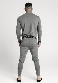 Graues Langarmoberteil und passende Jogginghosen mit einem subtilen Muster aus kleinen Designs. Schwarzer Gummibund mit dem Aufdruck 'SIKSILK'.