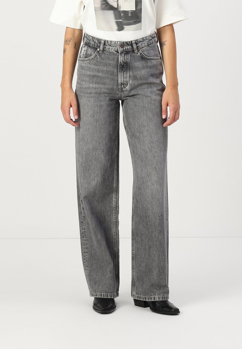 Harmaat leveälahkeiset farkut korkealla vyötäröllä, joissa on klassinen viiden taskun malli ja hillityt kulutuskuviot.