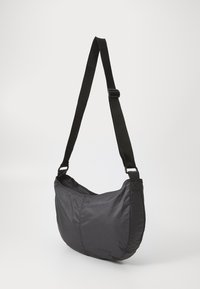Čierna nylonová taška cez plece s zakriveným tvarom, nastaviteľným popruhom, zipsovým uzáverom a hladkou textúrou. Minimalistický dizajn bez ďalších akcentov.