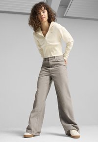 Felpa gialla chiaro con zip abbinata a jeans grigi a gamba larga e sneaker color crema. Capelli ricci, sfondo neutro.