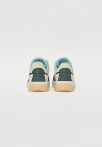 Low-top sneakers in cream, navy, and teal. Features a textured back, padded collar, and light brown rubber sole. Minimalist design.