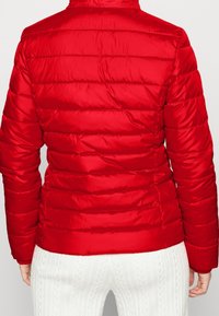 Červená péřová bunda s horizontálně prošívanými sekcemi, vysokým límcem a hladkou, lesklou texturou tkaniny. Elastické rukávy a lem.