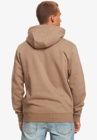 Brown cotton hoodie with a large hood, ribbed cuffs and hem, and a relaxed fit, viewed from the back. No visible logos or patterns.