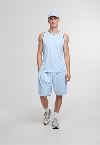 Lys blå atletisk tanktop med sort kant, matchende shorts og en lys blå kasket. Modellen bærer grå sneakers og hvide sokker.