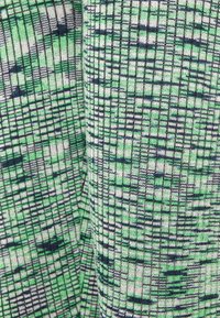 Tecido em malha nas cores verde, preto e branco, apresentando um padrão em grelha com texturas variadas, criando profundidade e interesse visual.