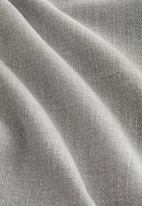 Tissu gris clair avec une texture fine et étroitement tissée, disposé en plis doux et délicats montrant une profondeur et des ombrages subtils.