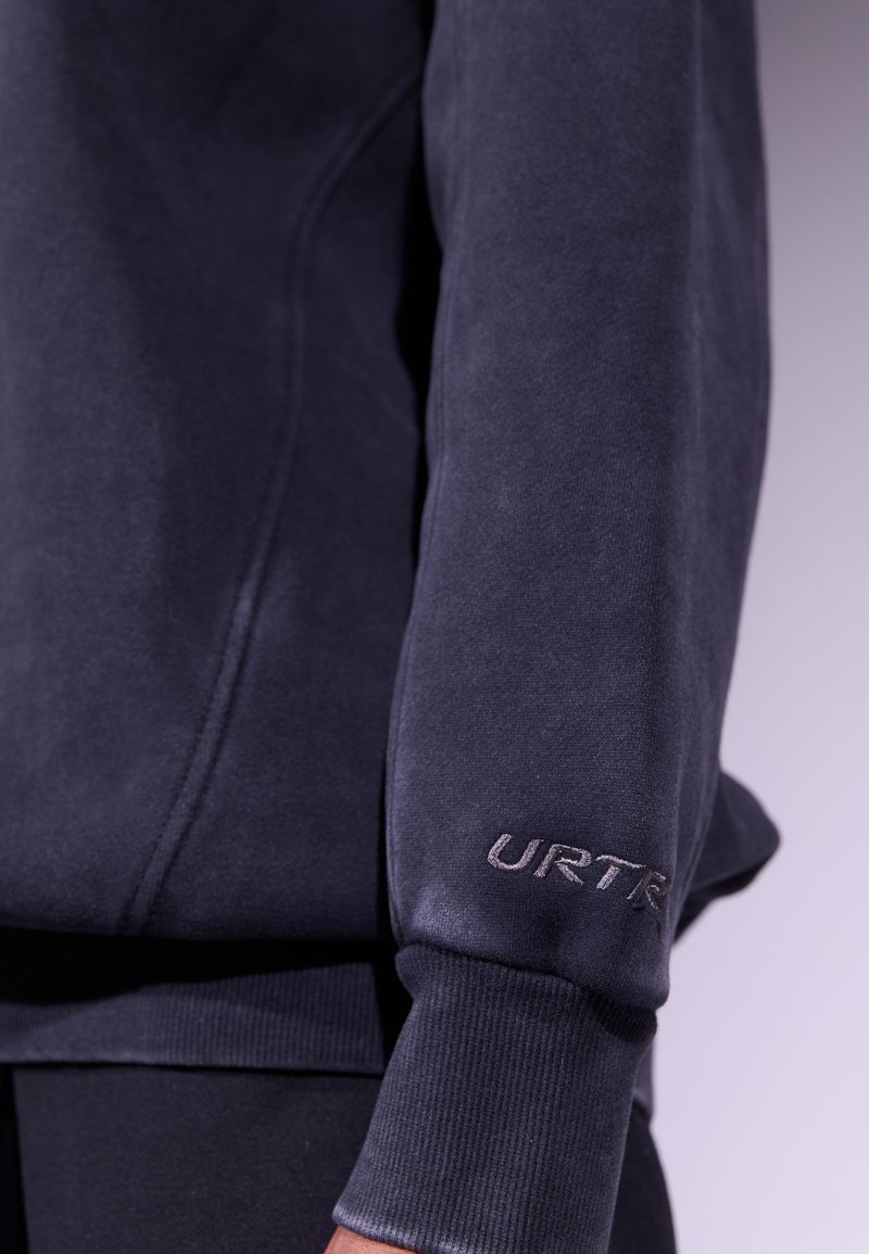 Sudadera de color azul marino oscuro con puños y dobladillo acanalados, que presenta un sutil logotipo bordado "URTR" en la manga. Textura suave y diseño atlético.