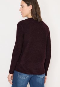 Bordeaux sweater van zacht, gestructureerd materiaal met lange mouwen en een ribbelrand. Gecombineerd met blauwe spijkerbroeken, gezien vanuit de achterkant.