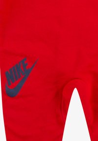 Crvene pamučne tajice s plavim Nike logotipom na lijevoj nozi. Dizajn uključuje suženi kroj i elastični pojas.