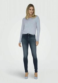 Suéter azul claro, jeans skinny de ganga e sapatos de salto azuis. Design ajustado, textura suave num conjunto casual. Aparência simples e moderna.