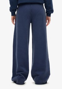 Granatowe spodnie o szerokich nogawkach wykonane z miękkiej tkaniny, z elastycznym pasem, luźnym krojem i subtelną fakturą. Widok z tyłu, pokazujący pełną długość.
