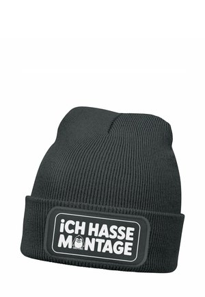 Black knit beanie with a ribbed texture. Features a rectangular patch in white with the text "iCH HASSE MONTAGE" and a cartoon penguin illustration.