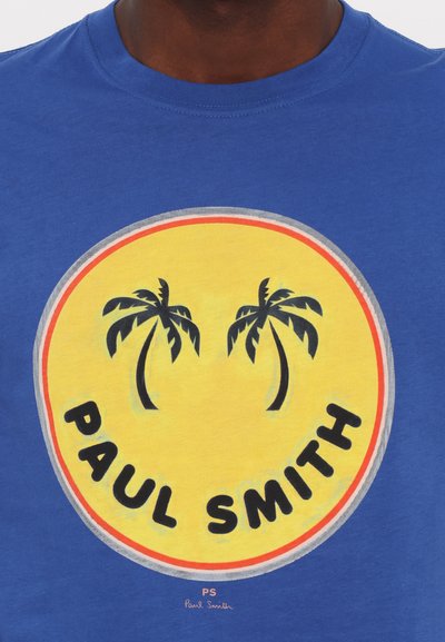 Zila kokvilnas T-kreklus ar lielu apļveida grafiku ar dzeltenu fonu, melnu tekstu "PAUL SMITH" un divām zaļām palmu kokiem.