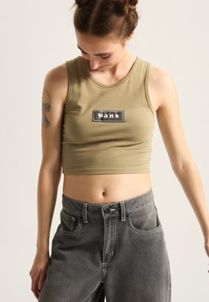 Top sin mangas de color verde oliva con un parche del logo de Vans en negro, combinado con pantalones de mezclilla gris de talle alto que tienen bolsillos delanteros y costuras en contraste.