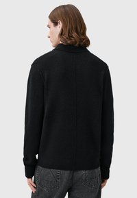 Mustavillainen villatakki, jossa on kaulus, ribattu hihansuu ja suora takasauma. Takki on pehmeä ja löysä istuvuus.