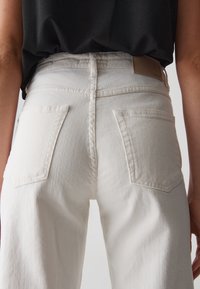 Jeans bianchi a vita alta con due tasche posteriori, caratterizzati da un tessuto testurizzato e da sottili dettagli di cucitura in vita e sulle tasche.