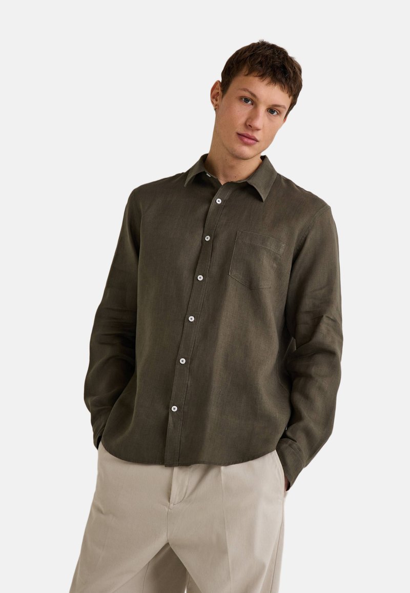 Chemise en lin vert olive à manches longues avec un col et des boutons blancs. Le tissu a une texture douce et un éclat subtil.