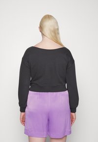 Sweatshirt preto cropped com uma gola larga, combinado com calções lilás que têm uma textura suave e um ligeiro brilho.
