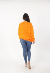 Feloranje gebreide trui met een oversized pasvorm, geribde manchetten en zoom. Gecombineerd met donkerblauwe skinny jeans en transparante hak sandalen.