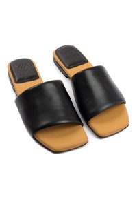 Sandali slide in pelle nera con una fascia ampia, design a punta quadrata e una soletta color tan. Accento sul tallone testurizzato in nero con dettaglio del logo.