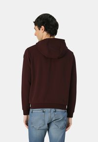 Felpa bordeaux con cappuccio regolabile con coulisse, texture morbida, polsini e orlo a costine, abbinata a jeans in denim azzurro chiaro con tasche posteriori.