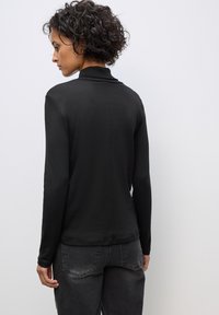 Maglietta nera a maniche lunghe con colletto, tessuto liscio, design aderente e cucitura centrale. Abbinata a jeans grigi, leggermente sbiaditi.