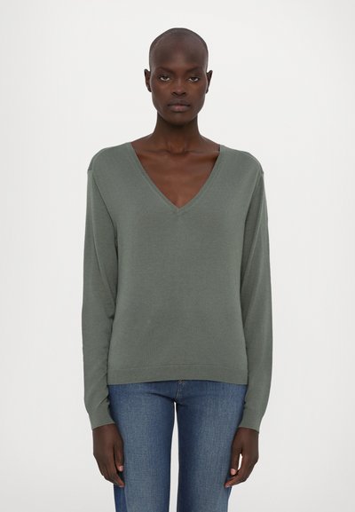 Suéter verde de manga larga con escote en V, textura de punto y puños acanalados. Combinado con jeans azules de corte recto para un look completo.