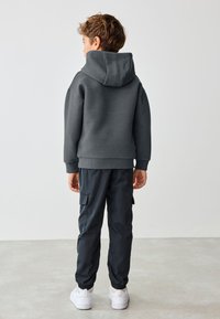 Grå tekstureret hættetrøje med stor hætte, kombineret med mørke cargobukser og hvide sneakers; bemærkelsesværdig for sit sporty, afslappede design.