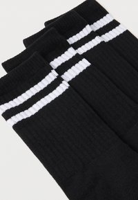 Sorte sokker med en ribbet tekstur, der har to hvide horisontale striber nær toppen. Fire par er stablet sammen.