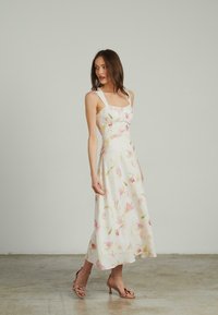 Blumenmidikleid mit quadratischem Ausschnitt, weißer Stoff mit rosa und grünen Mustern und breiten Trägern. Kombiniert mit Blush-Absätzen.