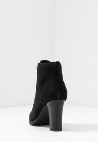 Botín de ante negro con un tacón afinado, una textura suave y una puntera redondeada. Presenta una silueta elegante y detalles de costura mínimos.