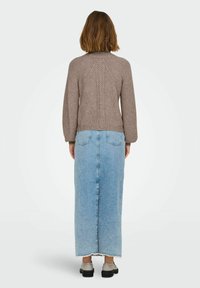 Maglione a coste marrone con maniche a sbuffo. Abbinato a una gonna di jeans lunga, blu chiaro, con orlo grezzo. Indossato con scarpe grigie.