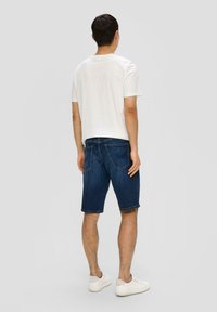 Shorts en denim bleu foncé avec une coupe régulière, dotés de deux poches arrière, d'un ourlet retroussé, et associés à un t-shirt blanc uni à manches courtes.