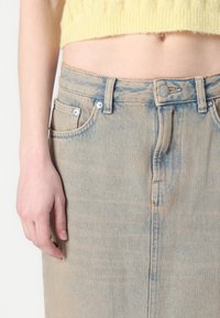 Fustă din denim de culoare bleu deschis, cu talie înaltă, buzunare frontale și închidere cu nasture. Materialul are o textură ușor decolorată și o croială dreaptă.