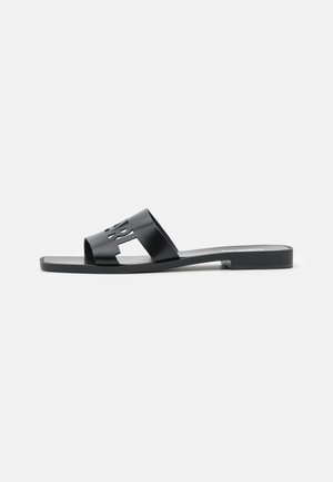 Black slide sandals with a cutout design featuring a prominent logo, flat sole, and smooth, glossy finish. Minimalist style.