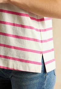 Puuvillane T-särk, millel on valge taustal horisontaalsed roosad triibud, küljeõmblus ja tekstureeritud kangas. Ühendatud siniste teksadega.