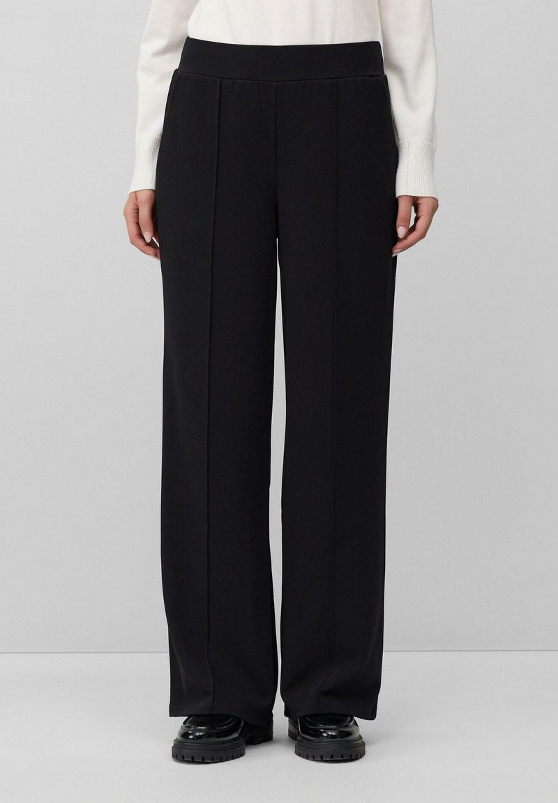 Zwarte wijde broek gemaakt van een gladde stof met een hoge taille en voorplooien, gecombineerd met glanzende zwarte plateauschoenen.