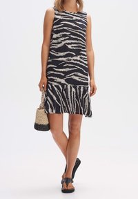 Bezramenné šaty s černobílým zebřím vzorem, s rozšířeným lemem. Nosené s tkanou taškou a černými sandály.