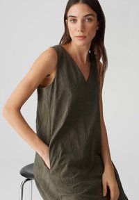 Olive green sleeveless dress with a V-neck, featuring a textured leaf pattern and side pockets. Smooth fabric, loose fit.