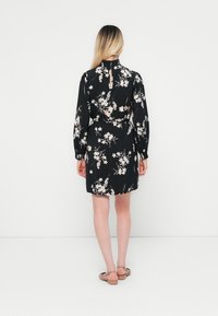 Vestido preto floral com mangas longas, um recorte nas costas e uma cintura ajustada. O tecido apresenta padrões florais em rosa e branco.