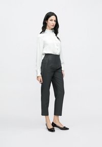 Balta blūze ar garām piedurknēm un volānu detaļām, tumši pelēkas augsta vidukļa bikses ar priekšējām šuvēm, kā arī melnas lakādas dzīvokļi ar lokveida akcentiem.