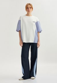 Camiseta blanca de gran tamaño con mangas de rayas azules y texto; combinada con pantalones de pierna ancha azul marino con rayas laterales de color azul claro.