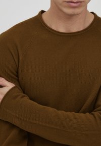 Brown textured long-sleeve shirt with a round neckline and raglan sleeves, featuring a subtle waffle knit pattern.