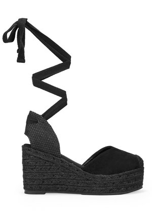 Sandalia de cuña espadrille negra con un tacón de tejido texturizado y un diseño de tiras cruzadas. Fabricada con material de ante.